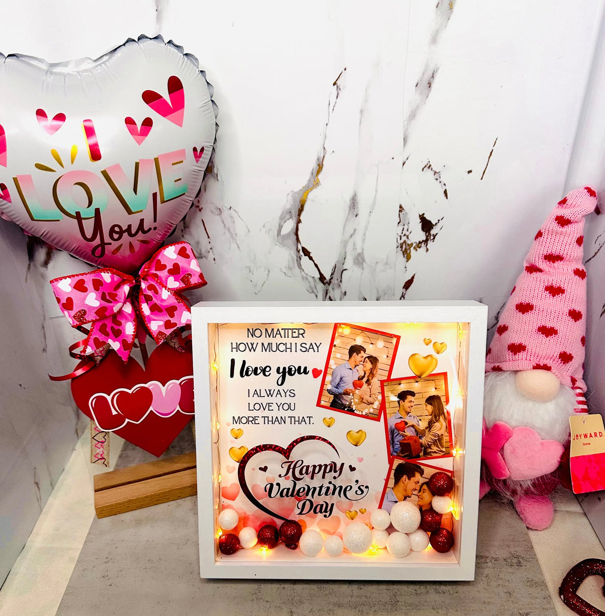 A curated Valentine's Day gift display featuring a heart-shaped 'Love You' balloon with a pink bow, a personalized LED photo shadow box with rose petals, and a plush gnome, showcasing romantic handmade gift ideas