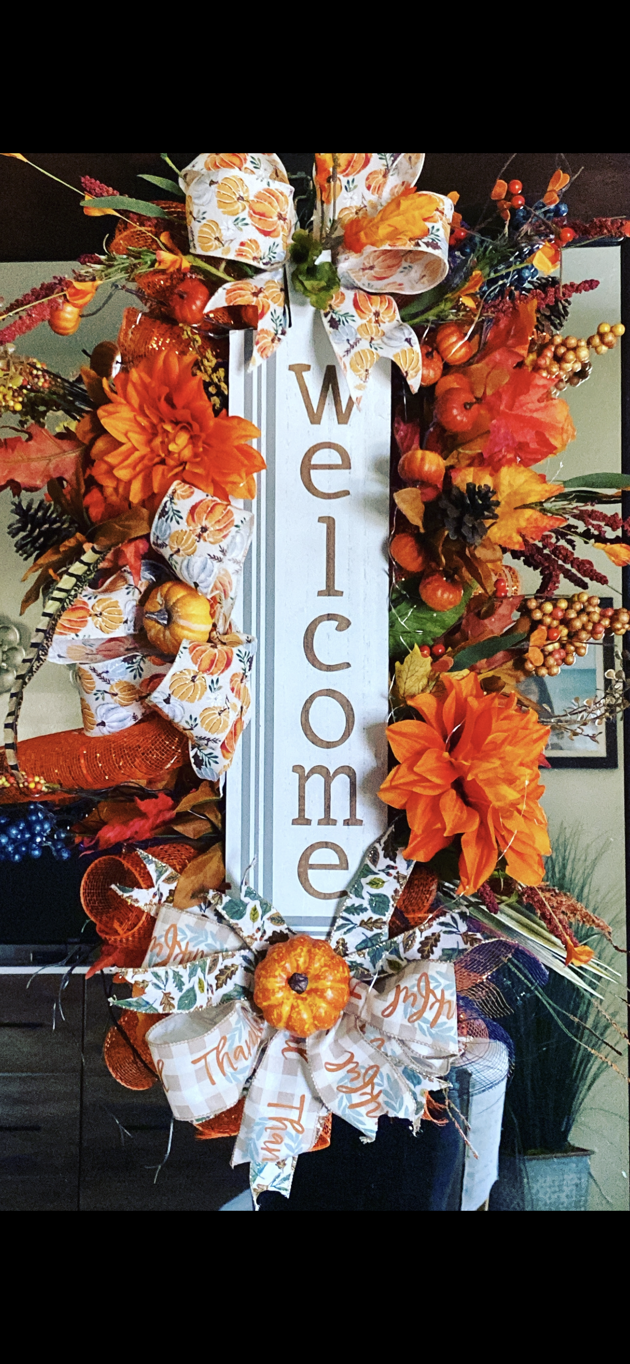Close-up of designer pumpkin and buffalo-check ribbon, orange dahlia, and berry accents on a handmade fall wreath