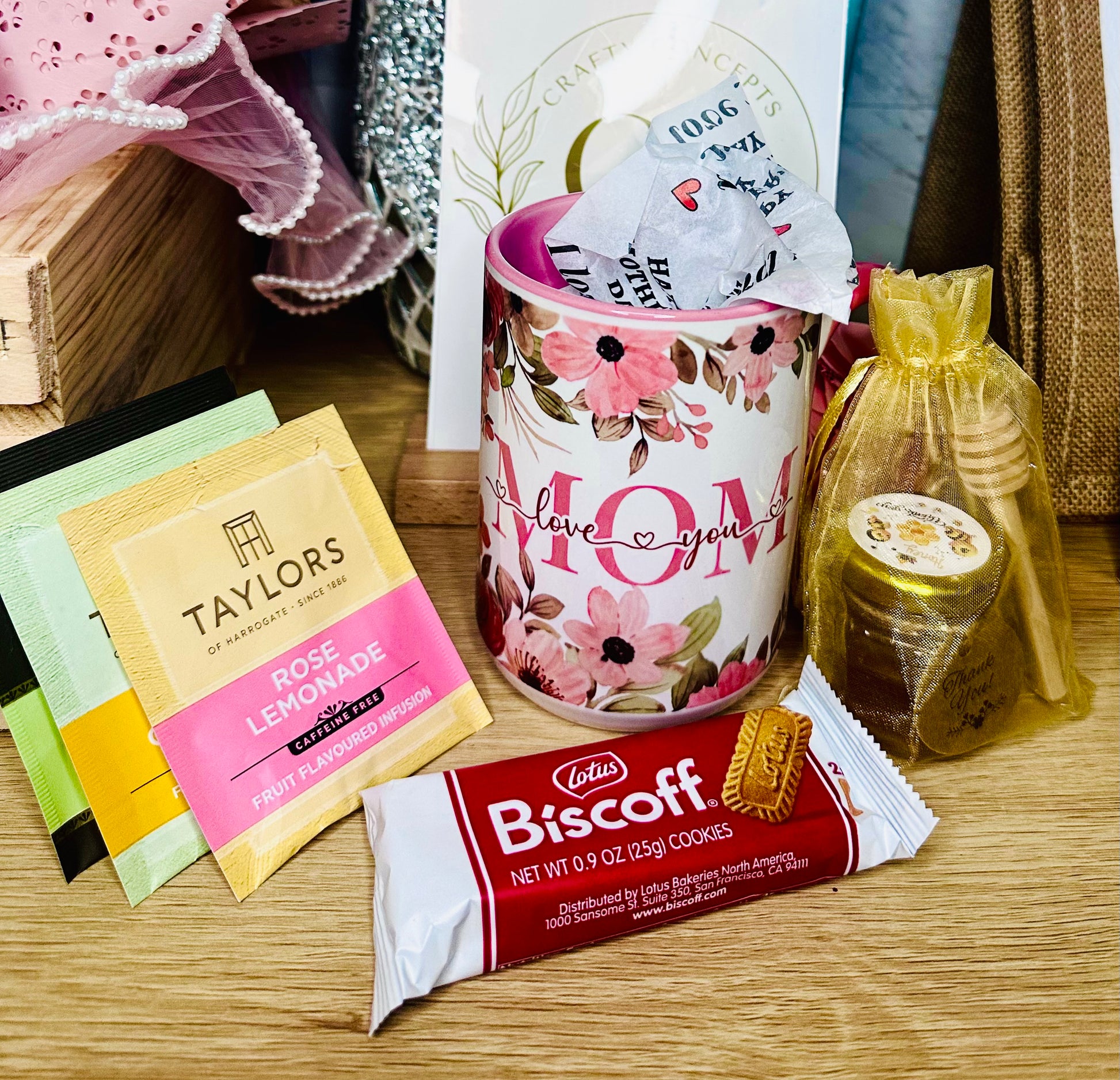 Mother's Day gift set with floral mom mug, tea assortment, honey jar, and Biscoff cookies for a cozy self care gift box.