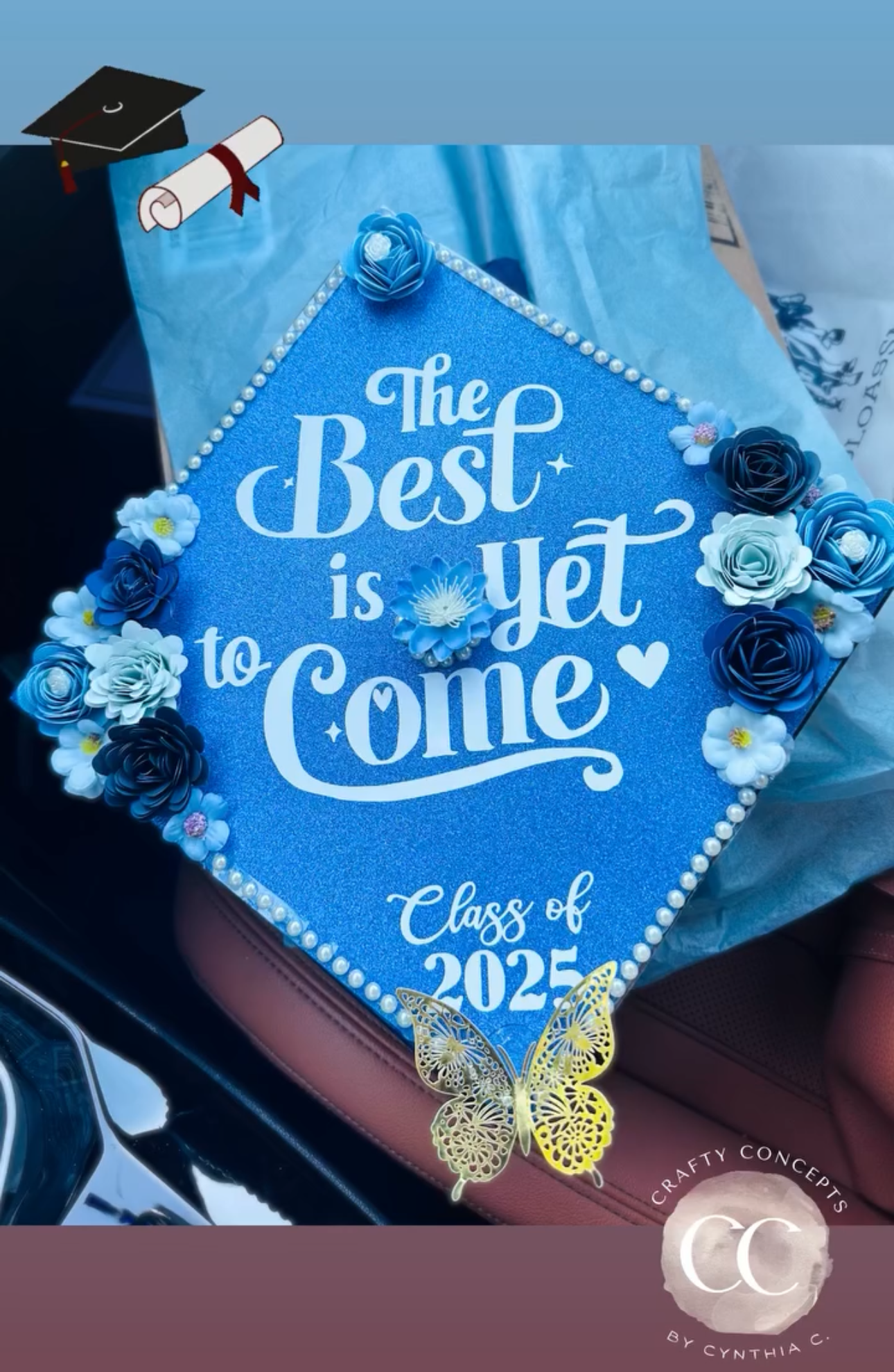 Blue floral cap: Blue glitter graduation cap topper with 3D paper flowers, pearl border and gold butterfly reading The Best is Yet to Come Class of 2025