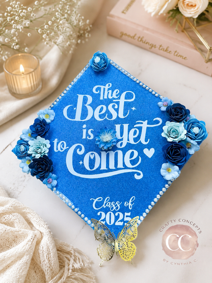 Blue floral cap: Blue glitter graduation cap topper with 3D paper flowers, pearl border and gold butterfly reading The Best is Yet to Come Class of 2025