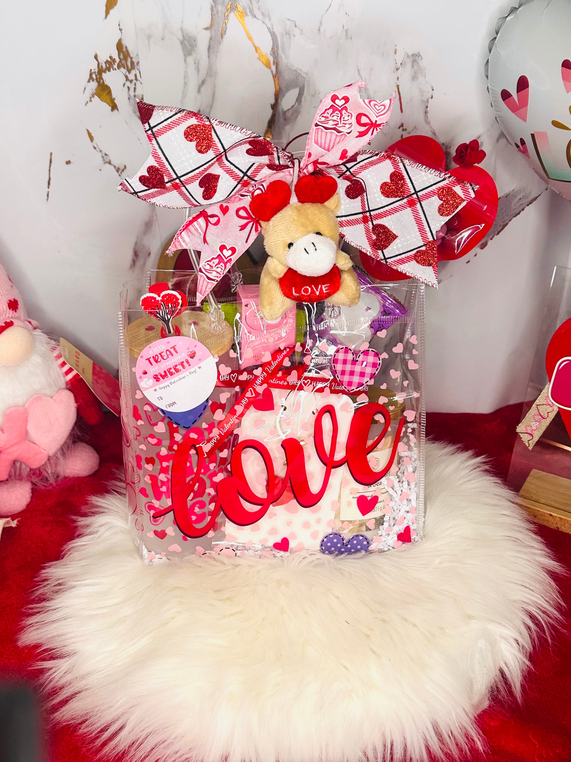 Valentine’s Day gift bundle featuring a 'Love More Worry Less' frosted glass tumbler with bamboo lid, a white Threshold candle, Lindt truffles, pistachios, snacks, and a pink gnome plush on a red background