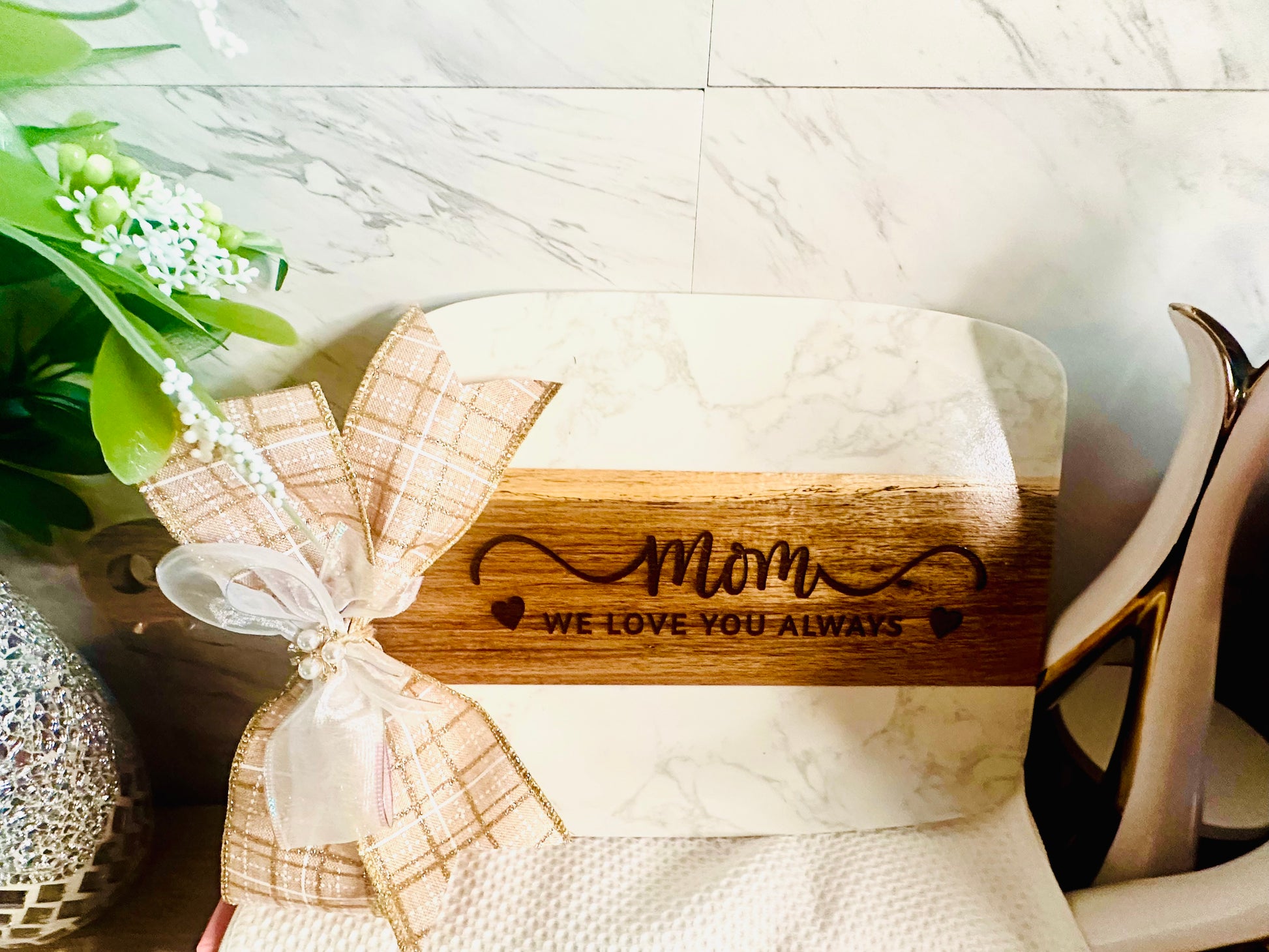 Luxury gift presentation of a personalized marble and wood cutting board expertly decorated with a large, rustic burlap bow and floral accents.