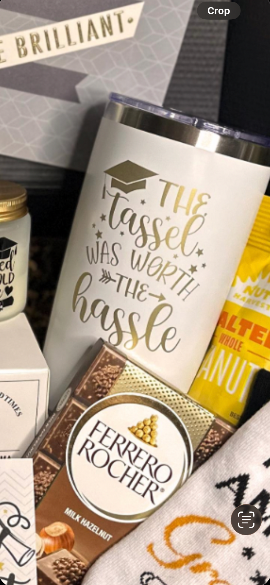 Close-up of white insulated tumbler laser engraved with The Tassel Was Worth the Hassle surrounded by chocolates and grad socks