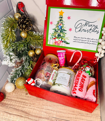 Christmas gift box with festive items including a candle, mug, and card on a wooden surface.
