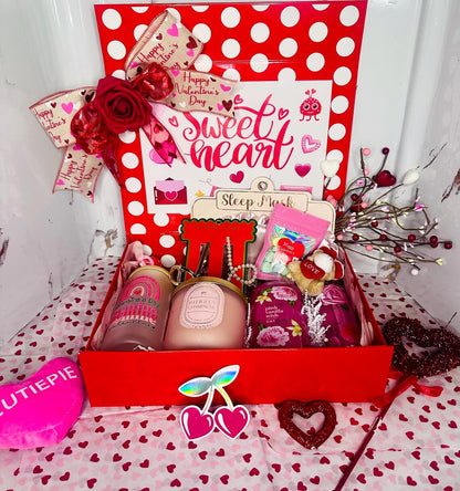 A curated Valentine's Day luxury gift box featuring a "Sweetheart" themed red and white polka-dot box, containing a pink champagne candle, a frosted glass tumbler with a bamboo lid, a plush "LOVE" teddy bear, and spa products.