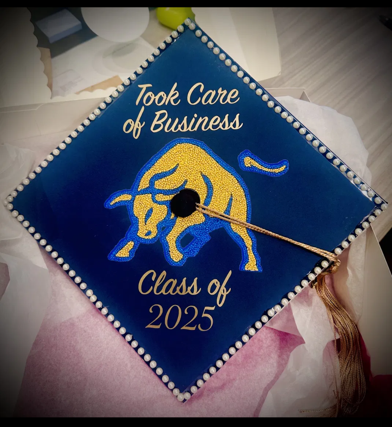 Navy graduation cap topper with gold and blue chenille bull patch, pearl trim and gold lettering reading Took Care of Business Class of 2025