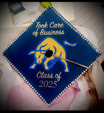 Navy graduation cap topper with gold and blue chenille bull patch, pearl trim and gold lettering reading Took Care of Business Class of 2025
