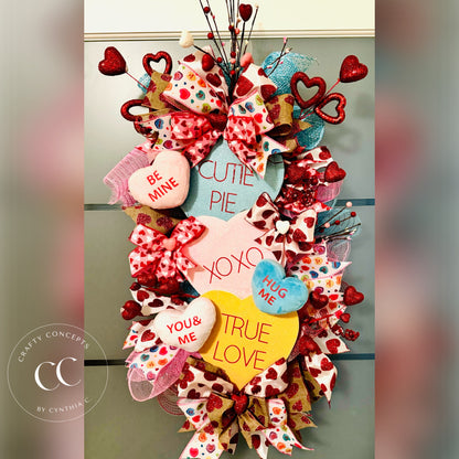 Vertical Valentine's Day teardrop swag with colorful conversation hearts, designer bows, and a green lollipop.