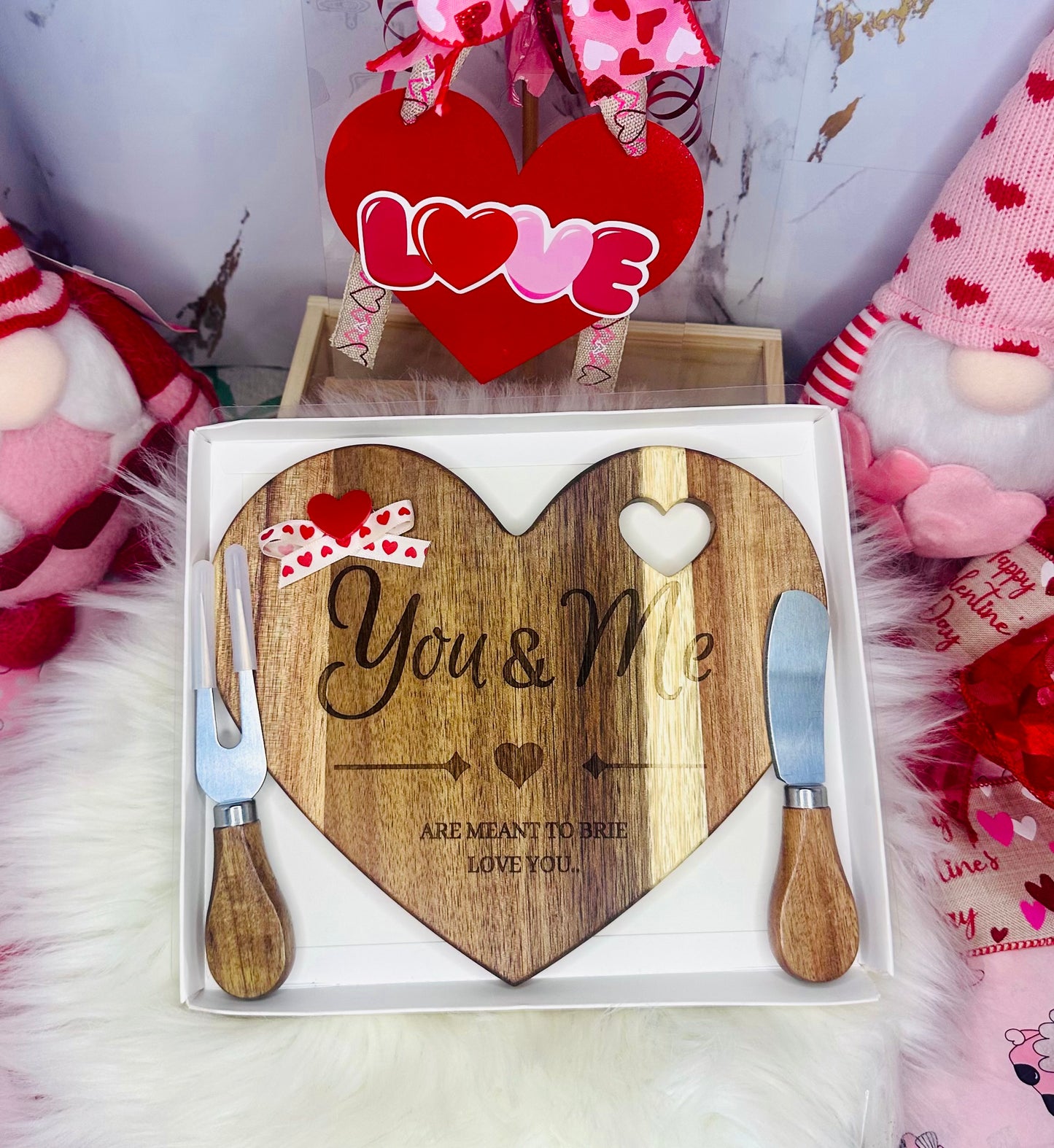 Heart-shaped wooden cutting board engraved with "You & Me," featuring two matching cheese knives in a white gift box