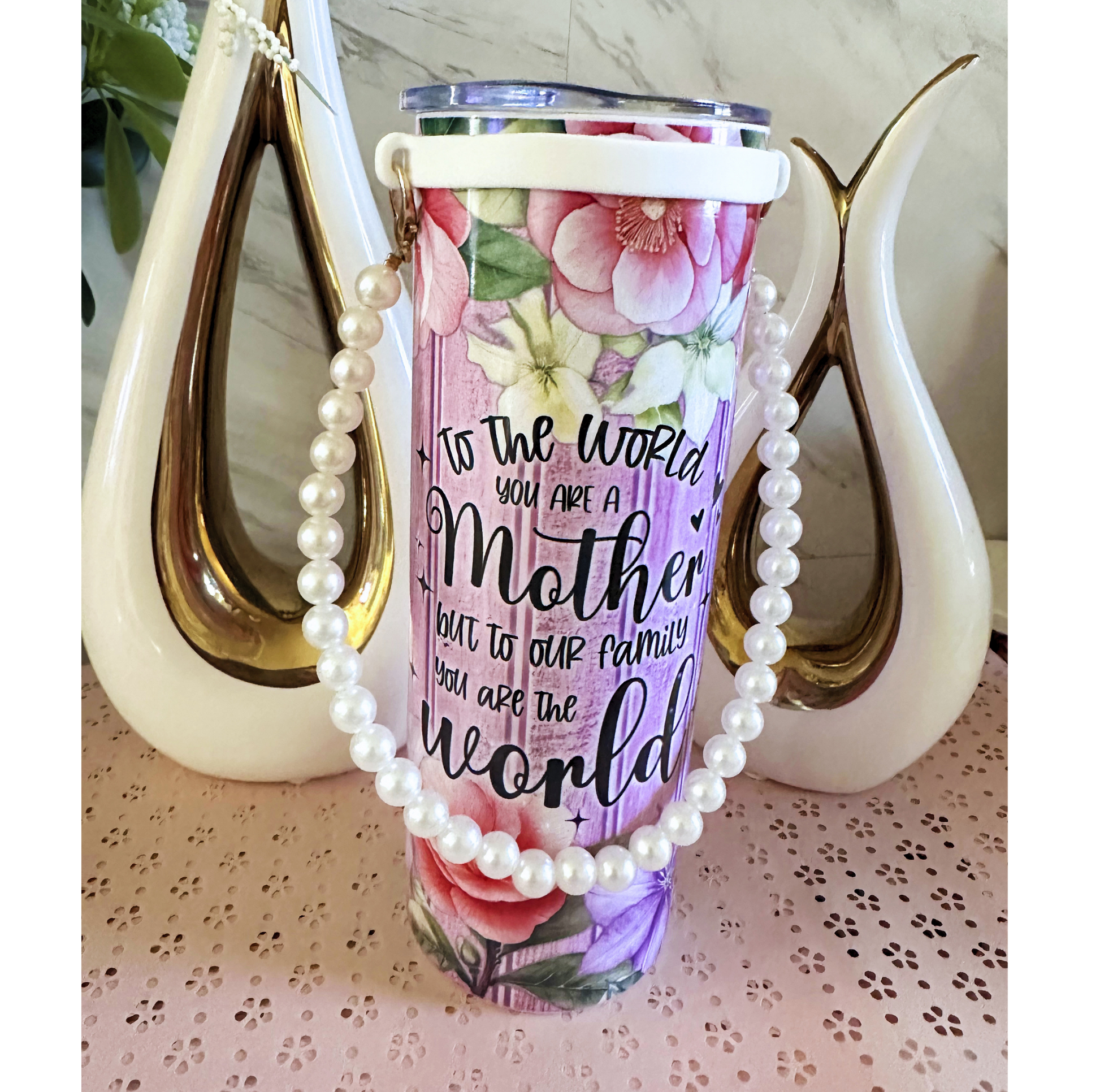 Tumbler with floral design and text, draped with pearls.